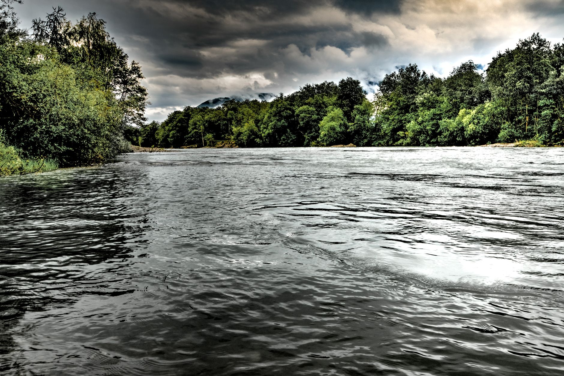 A scenic river view surrounded by lush trees under moody skies.